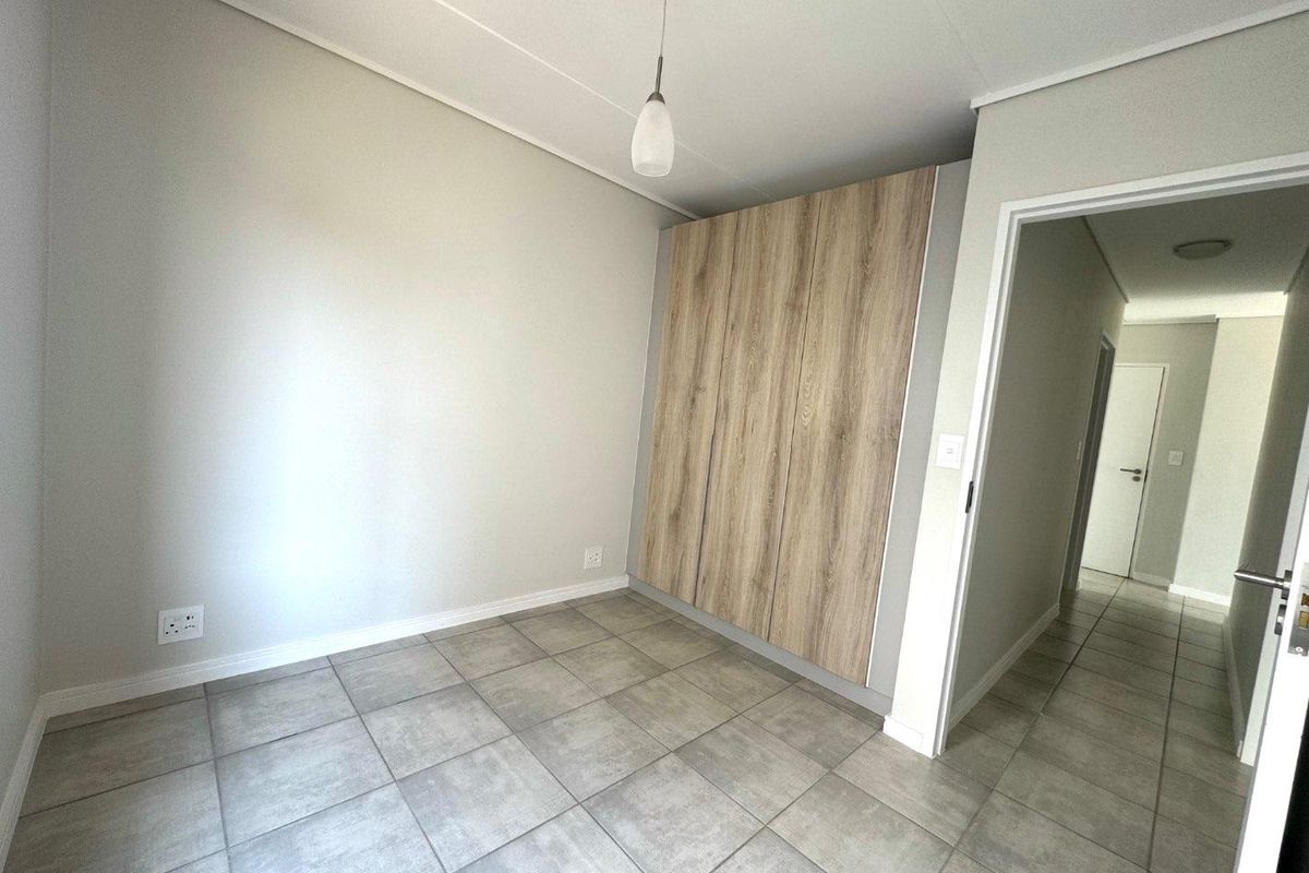 A clean, empty bedroom featuring modern wood-finish built-in cupboards, neutral grey tiled flooring, and a simple pendant light fixture.