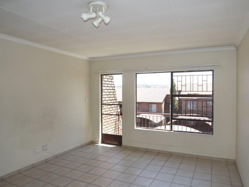 An empty living room featuring tiled flooring, security bars on the windows, and a security gate leading to an outdoor area.