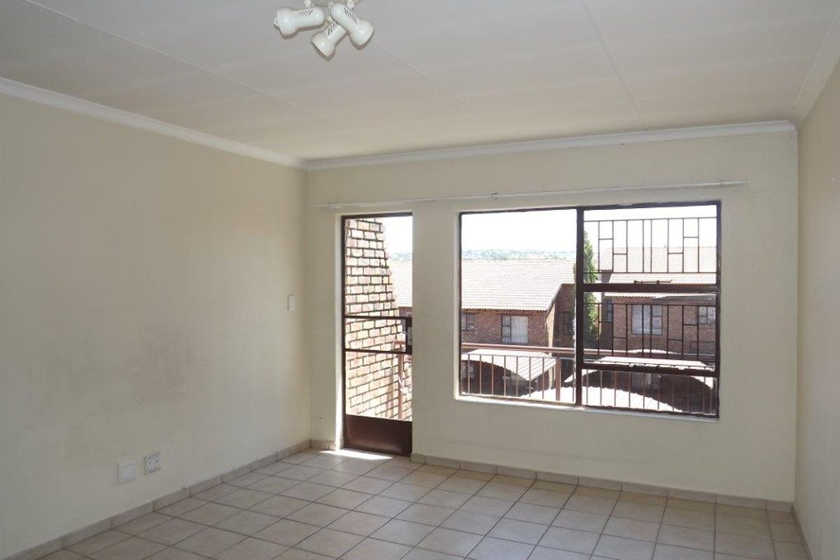 An empty living room featuring tiled flooring, security bars on the windows, and a security gate leading to an outdoor area.