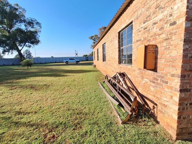 Rear exterior view of the industrial property featuring exposed brickwork, steel-framed windows, and a large surrounding grass area.