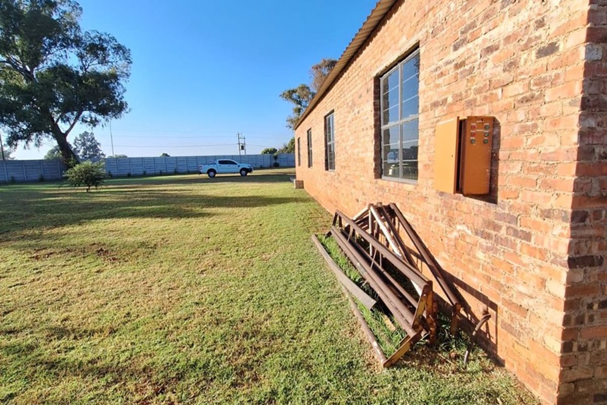 Rear exterior view of the industrial property featuring exposed brickwork, steel-framed windows, and a large surrounding grass area.