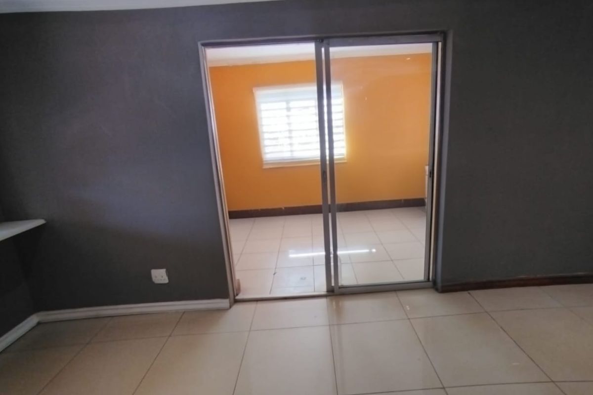 An interior view showing a tiled living area with a sliding glass door leading to an adjacent room with orange walls and a window.