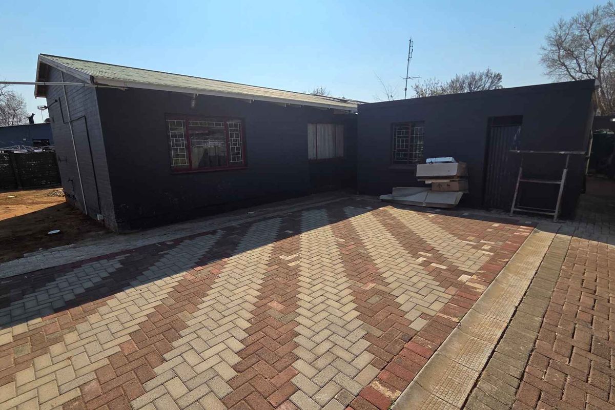 Rear exterior view of the property featuring a paved courtyard area and dark painted brick facade.