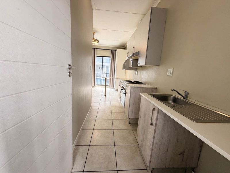 A functional galley-style kitchen featuring built-in cabinetry, a stainless steel sink, and integrated cooking appliances, leading towards a balcony area.