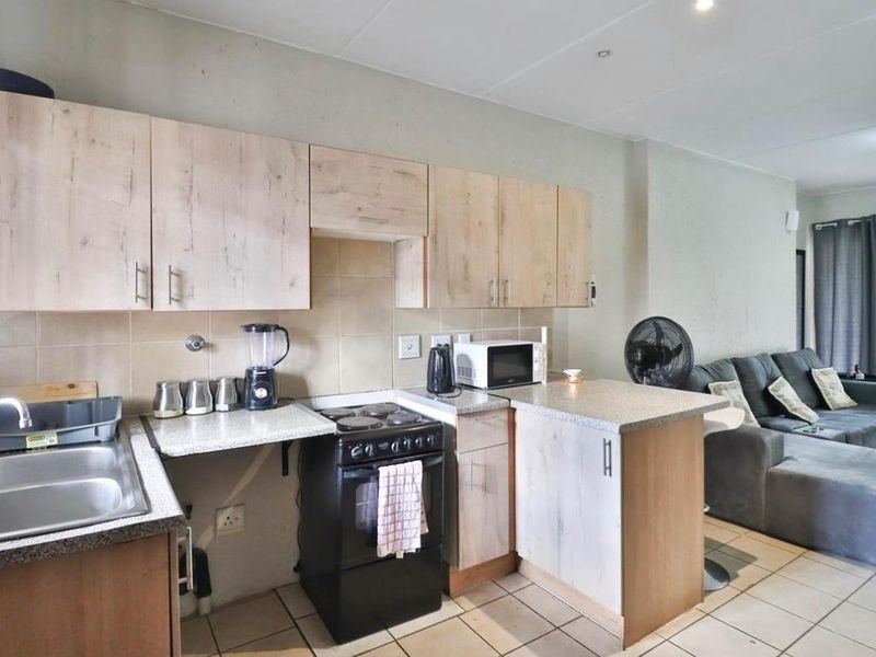 Open-plan kitchen and living area featuring light wood-finish cabinetry, laminate countertops, a double basin sink, and tiled flooring throughout.