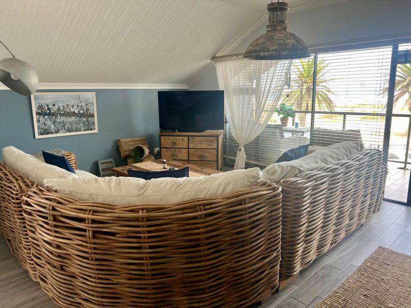 A comfortable living room featuring vaulted ceilings, tiled flooring, and large sliding glass doors that open onto a balcony with natural light.