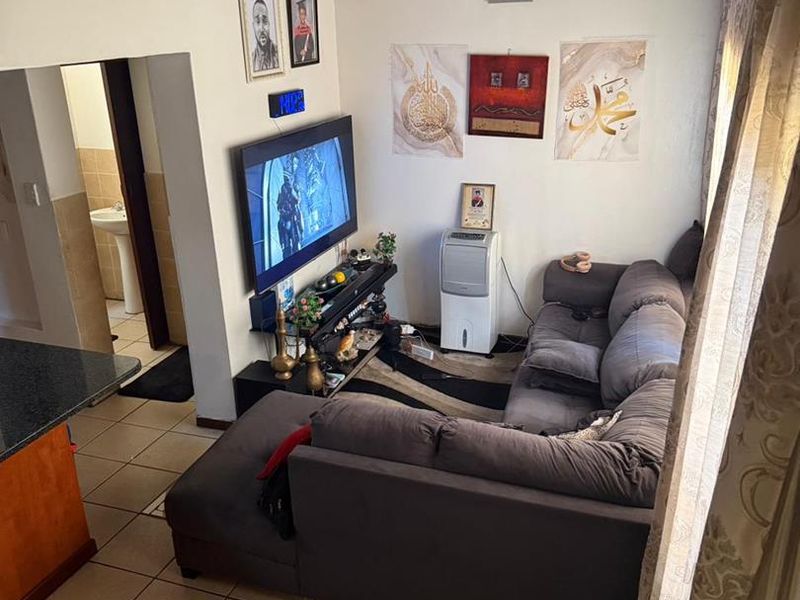 A compact living room featuring tiled flooring, a mezzanine level above, and direct access to an adjacent bathroom area.