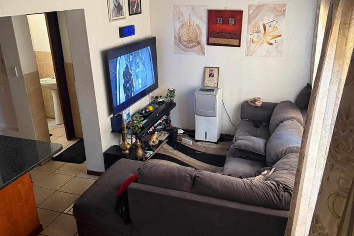 A compact living room featuring tiled flooring, a mezzanine level above, and direct access to an adjacent bathroom area.