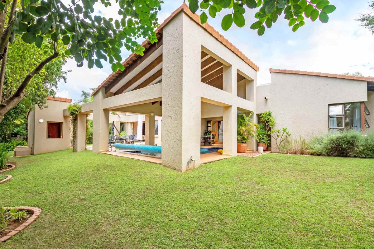 Spacious rear garden featuring a covered patio area with a swimming pool, set against the architectural facade of the house.
