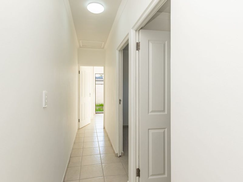 A clean, neutral hallway featuring tiled flooring and access to multiple rooms, providing a bright and functional transition space within the home.