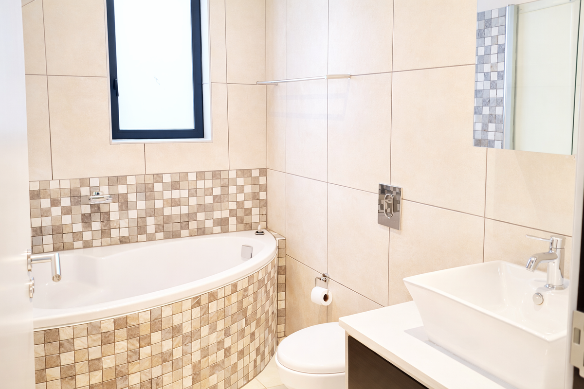 Modern bathroom featuring a corner bathtub with mosaic tile surround, a vessel sink vanity, and neutral wall tiling.