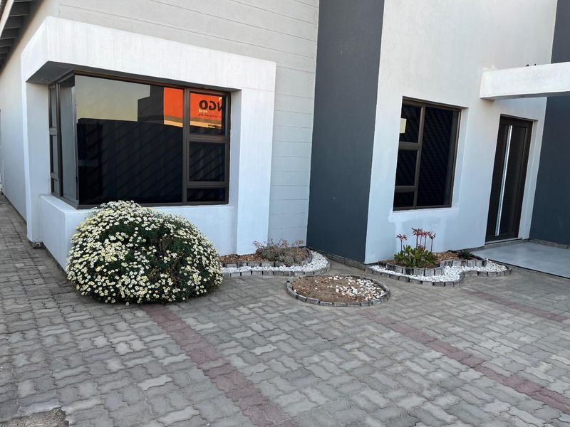 Modern front facade featuring paved driveway, clean architectural lines, and dark aluminium window frames with landscaped garden beds.