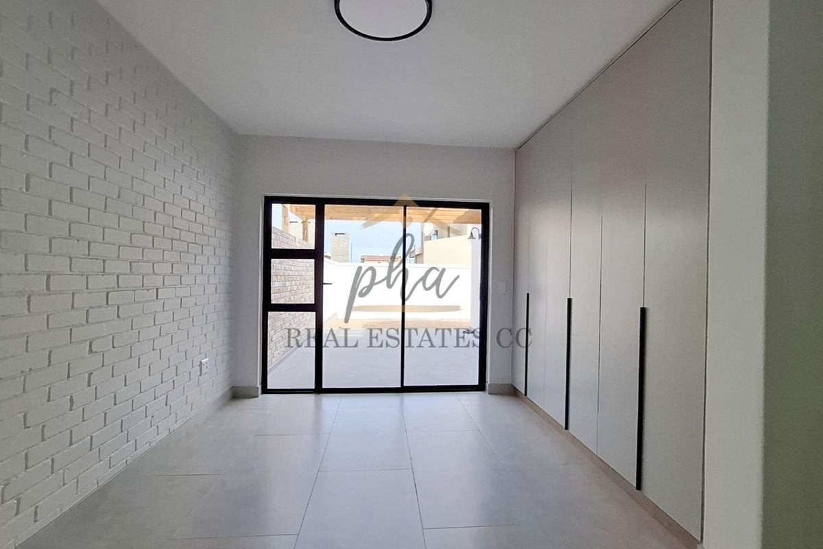 A bright, modern bedroom featuring built-in cupboards, a textured brick feature wall, large format floor tiles, and direct access to an outdoor patio area.