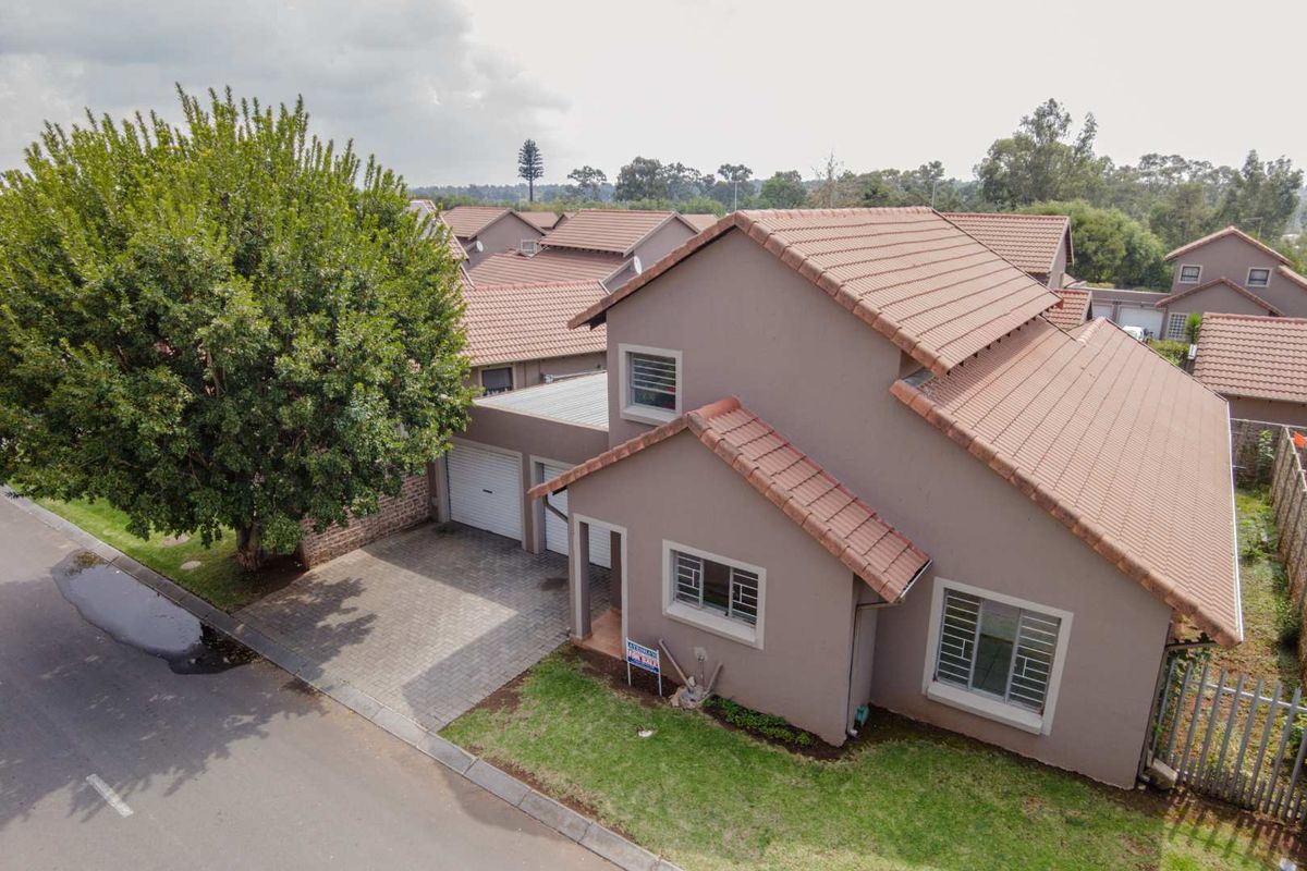 Aerial view of a townhouse featuring a tiled roof, paved driveway, double garage, and a small front garden area.
