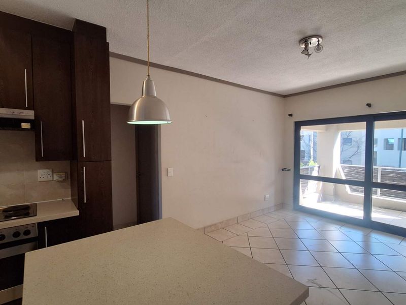 Open-plan kitchen and living area featuring dark cabinetry, stone countertops, tiled floors, and large sliding doors leading to a balcony.