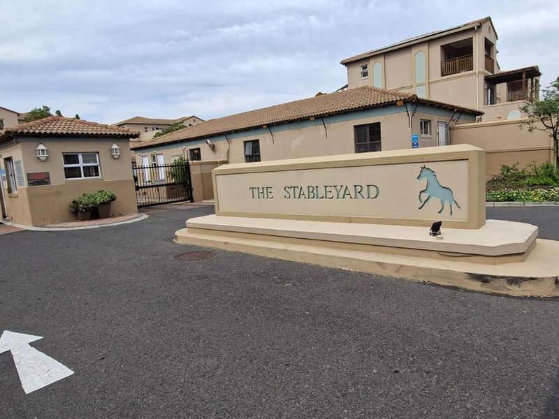 The entrance to The Stableyard apartment complex, featuring a secure gated access point, guard house, and paved driveway.