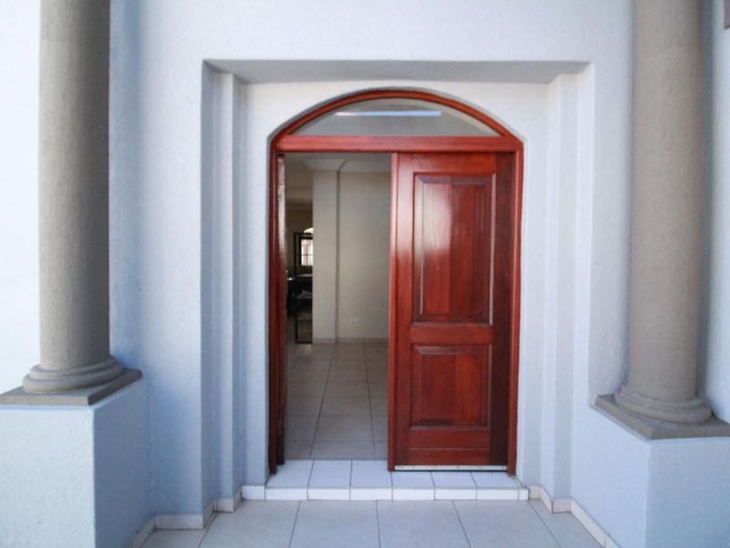 A welcoming front entrance featuring a solid wooden arched door with a fanlight, flanked by decorative columns and finished with tiled flooring.
