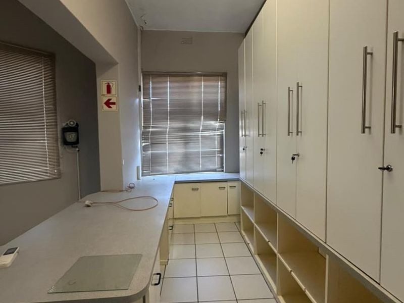 A functional scullery or utility space featuring extensive built-in cabinetry, laminate countertops, and tiled flooring, offering ample storage and workspace.