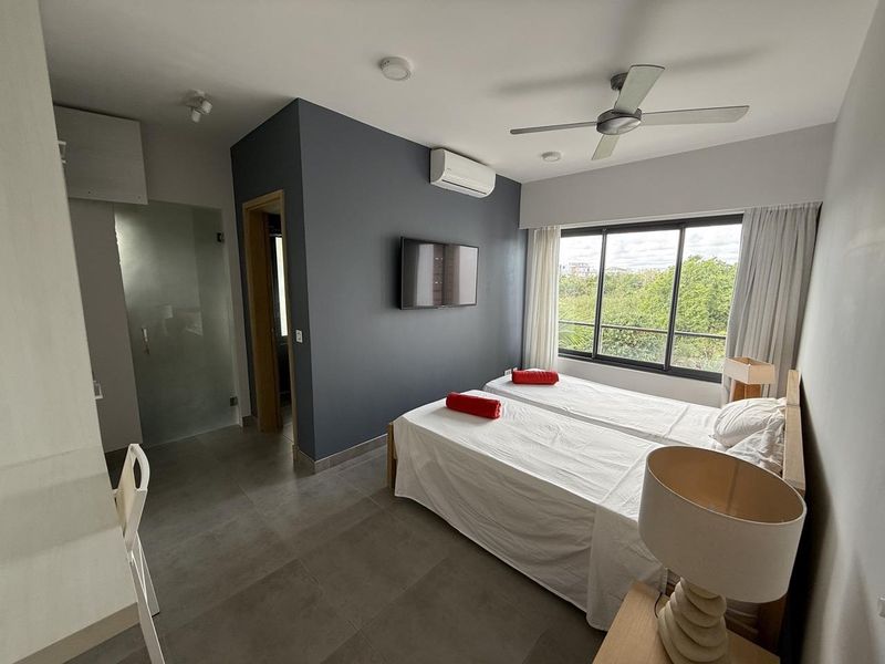 A modern bedroom featuring tiled flooring, a ceiling fan, split-system air conditioning, and an en-suite bathroom accessed via a frosted glass door.