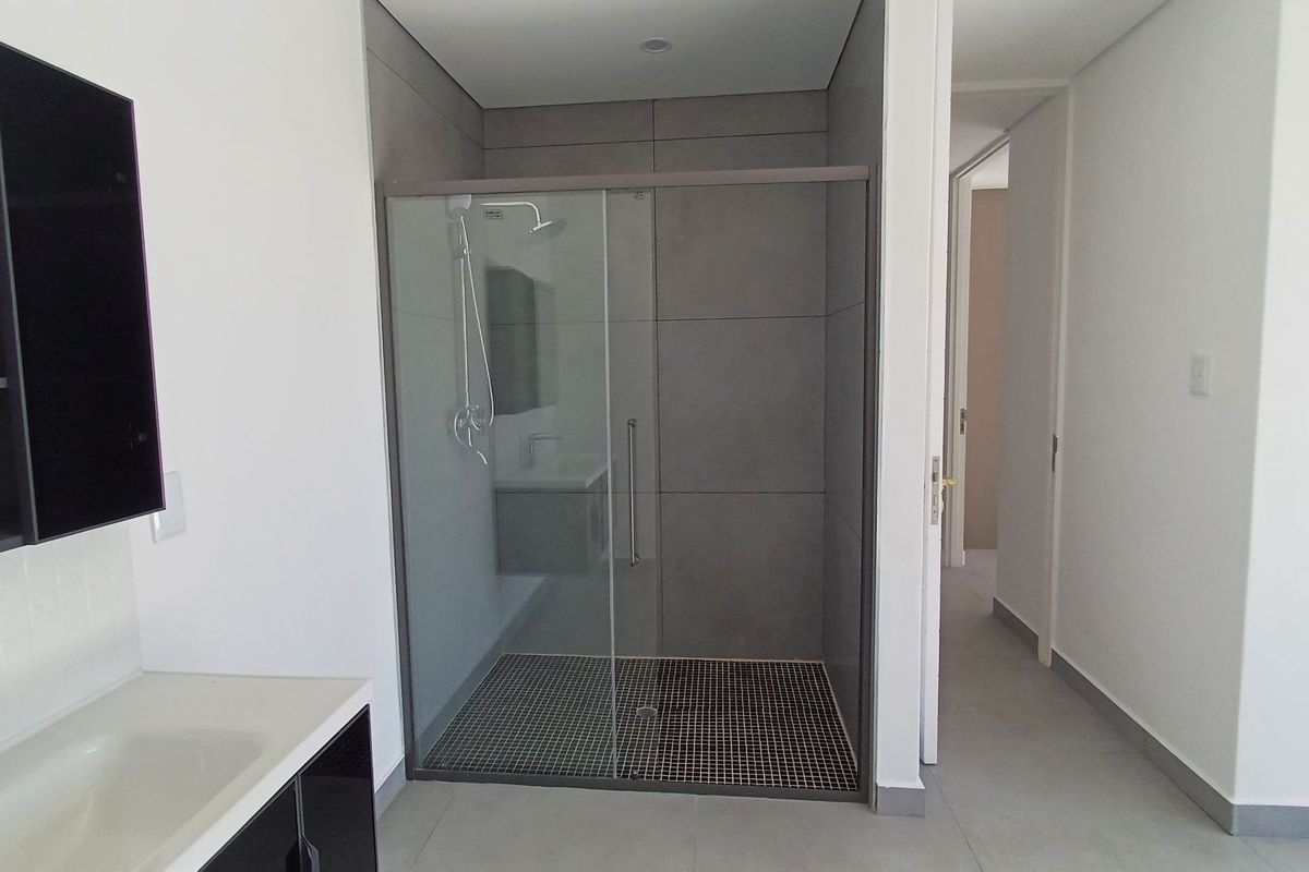 Modern bathroom featuring a walk-in shower with glass enclosure, contemporary vanity unit, and neutral large-format wall tiles.
