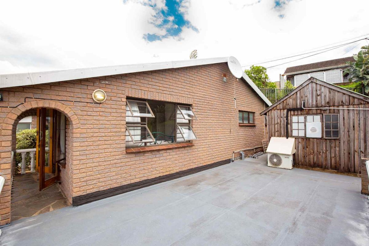 Rear exterior view featuring a brick facade, paved patio area, and a detached timber storage shed with an integrated air conditioning unit.
