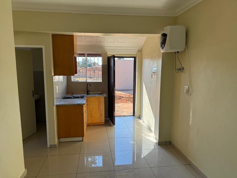 Open-plan kitchen area featuring tiled floors, built-in cabinetry, an electric hob, and direct access to the exterior.