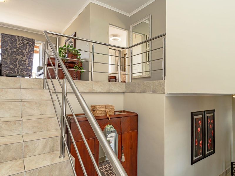 A bright hallway featuring a tiled staircase with a modern stainless steel balustrade leading to an elevated landing area.