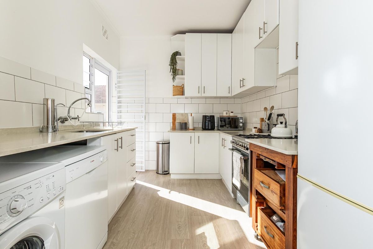 A bright, functional kitchen featuring white cabinetry, subway tile backsplash, light wood-look flooring, and integrated space for laundry appliances.