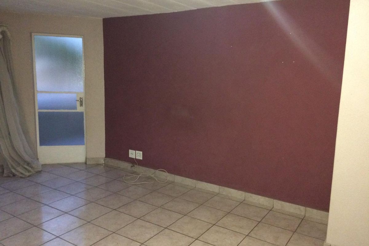 An empty living area featuring tiled flooring, a feature wall, and a frosted glass door leading to an exterior space.