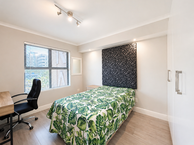 A well-maintained bedroom featuring laminate flooring, built-in wardrobes, track lighting, and a window with venetian blinds.
