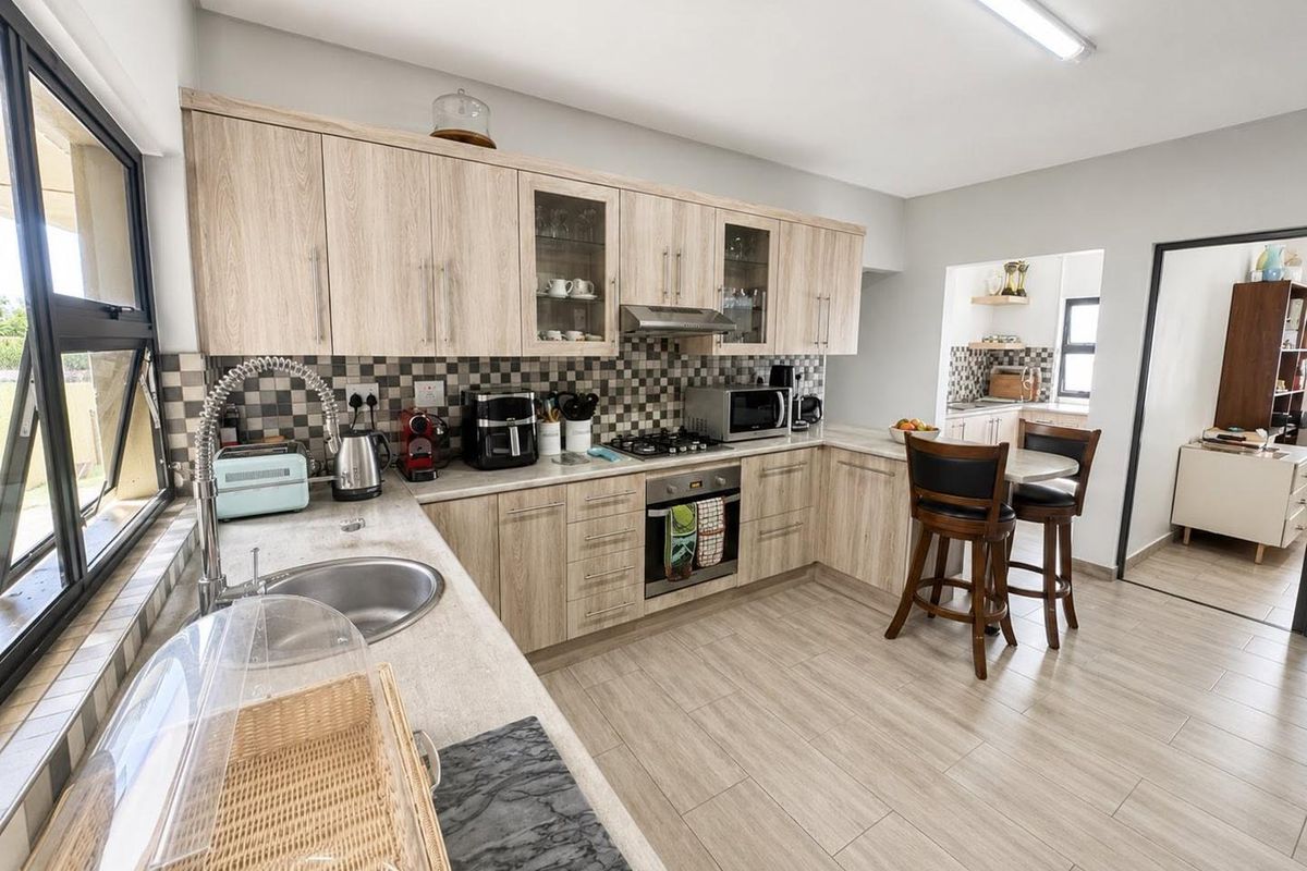 A functional kitchen featuring light wood-finish cabinetry, tiled backsplash, built-in oven with gas hob, and a stainless steel sink with a gooseneck faucet.