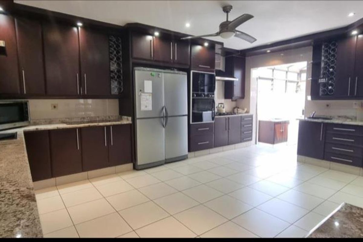 Spacious kitchen featuring dark wood cabinetry, granite countertops, tiled flooring, and built-in appliances including an oven and extractor fan.