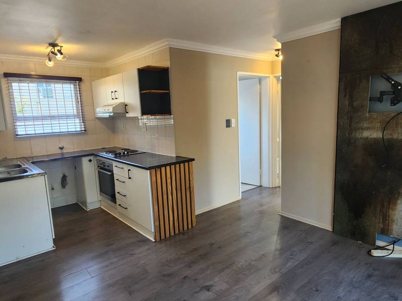 Open plan living and kitchen area featuring laminate flooring, built-in oven and hob, and a prominent feature wall with integrated TV mount.