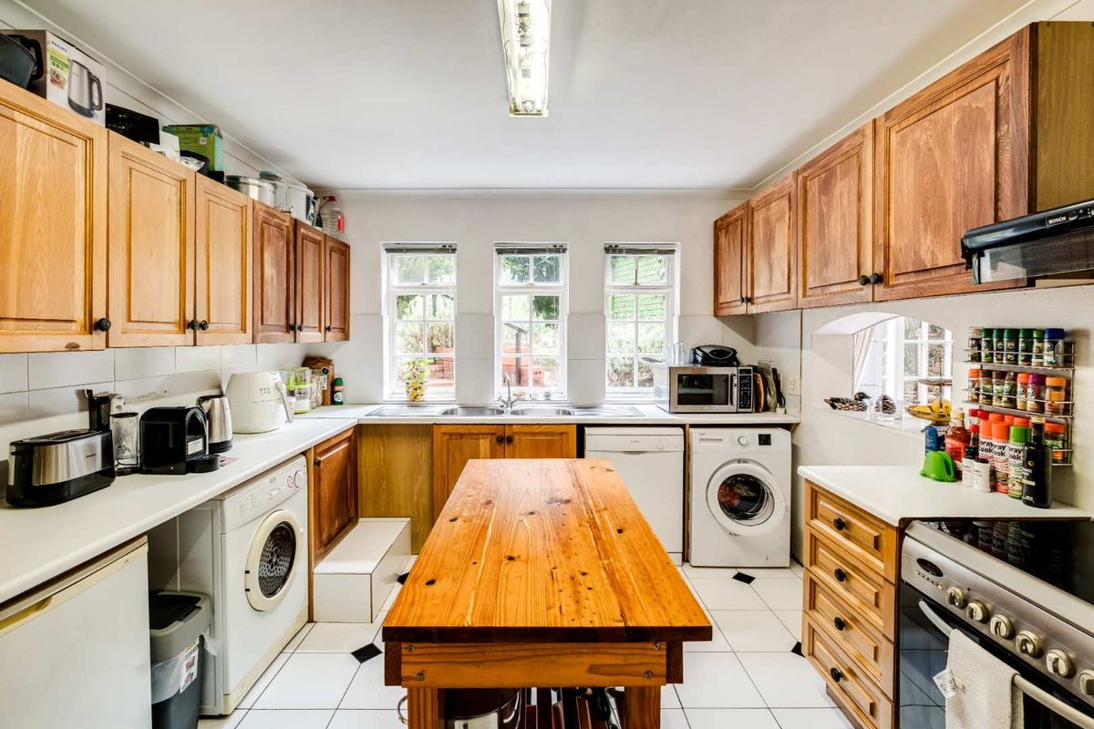 A functional kitchen featuring wooden cabinetry, tiled flooring, integrated appliances, and a central wooden island, offering a practical layout with ample storage space.