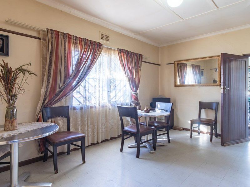 A living area featuring tiled flooring, cornice detailing, and window security bars, providing a functional space with potential for modern updates.