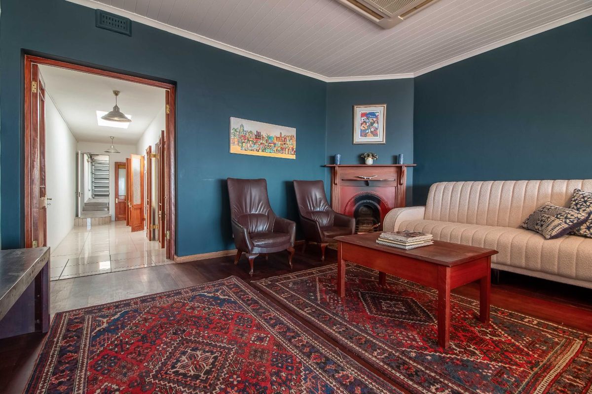 A cozy living room featuring a traditional fireplace, dark blue walls, timber flooring, and a view into the connecting hallway.