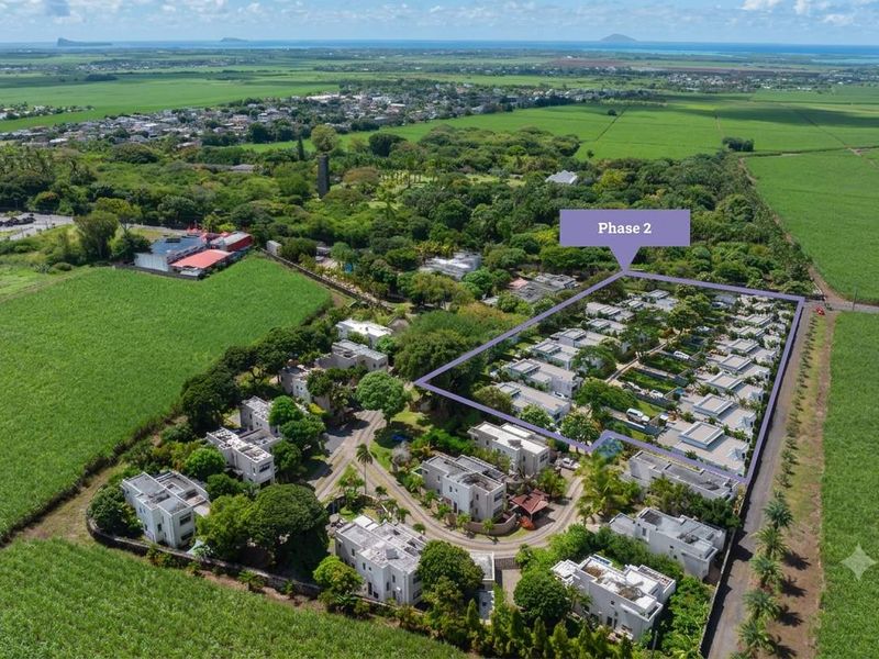 Aerial view of a residential townhouse development phase surrounded by lush green agricultural fields and coastal landscape.