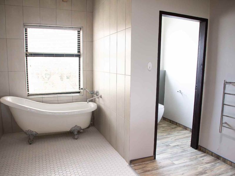 A bright bathroom featuring a classic clawfoot bathtub, neutral wall tiling, and a modern heated towel rail.