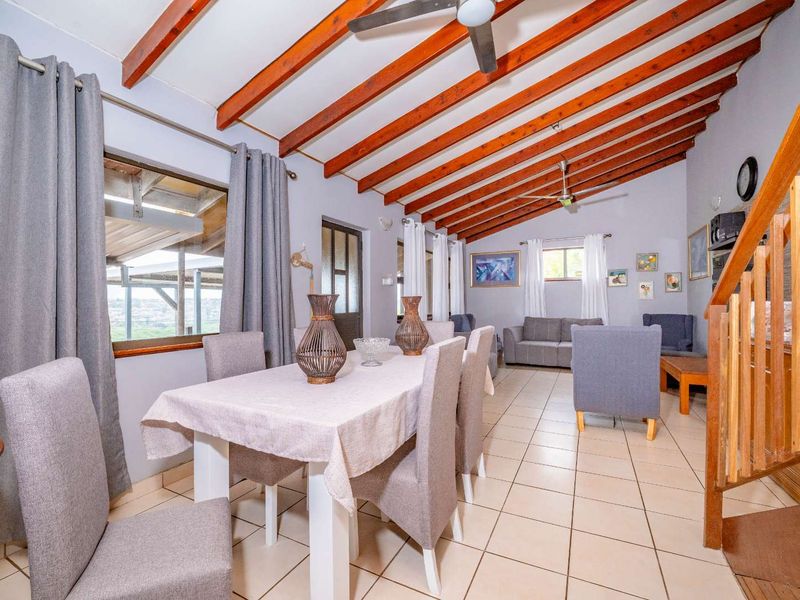 Spacious open-plan living and dining area featuring exposed timber ceiling beams, tiled flooring, and a timber staircase.