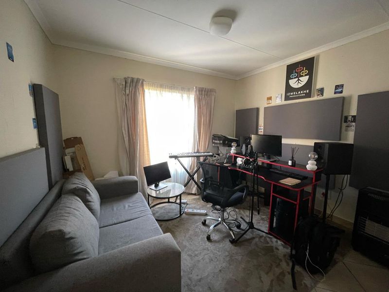 A multi-purpose bedroom space currently utilized as a home studio, featuring acoustic wall panels and natural light through a window with curtain tracks.