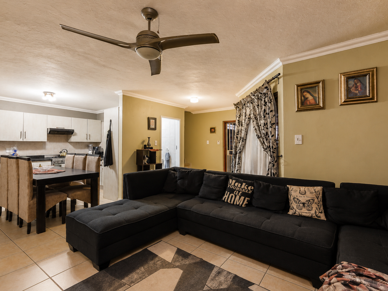 Open-plan living and dining area featuring tiled floors, a ceiling fan, and a functional kitchen with built-in cabinetry and an extractor fan.