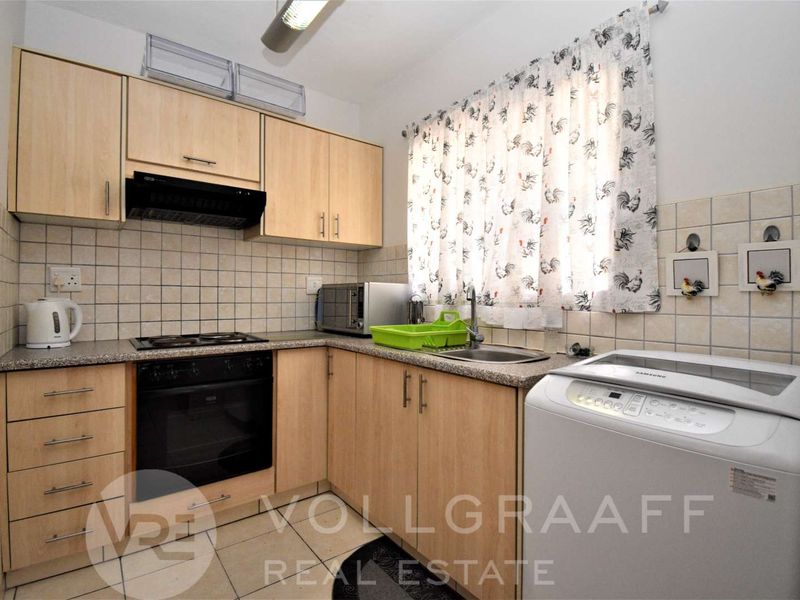 A functional kitchen featuring light wood-finish cabinetry, a tiled backsplash, built-in oven with hob, and a stainless steel sink.