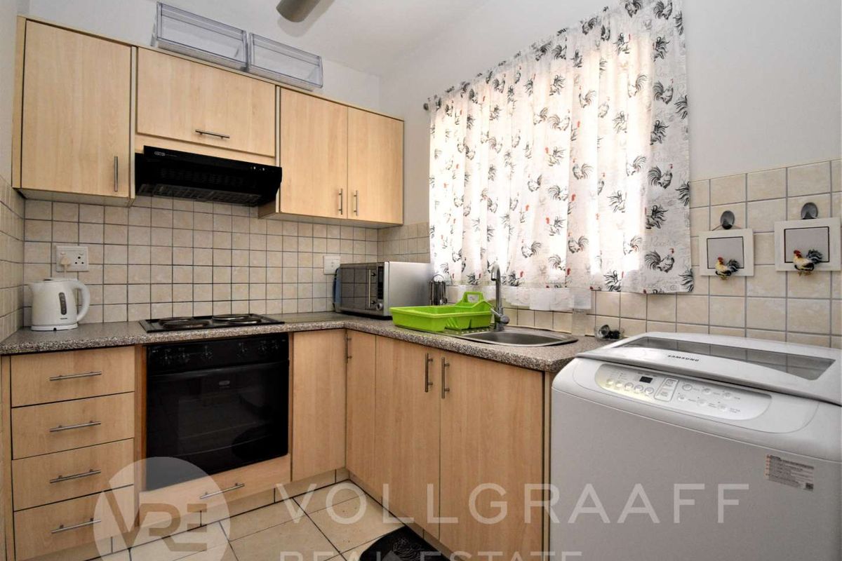 A functional kitchen featuring light wood-finish cabinetry, a tiled backsplash, built-in oven with hob, and a stainless steel sink.