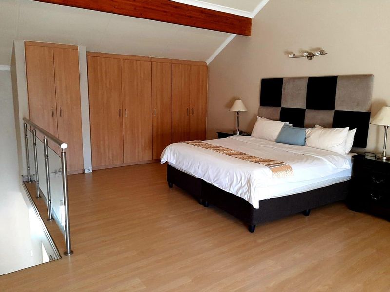 Spacious loft-style bedroom featuring vaulted ceilings, exposed timber beam, laminate flooring, and extensive built-in cupboard storage with a modern glass balustrade.