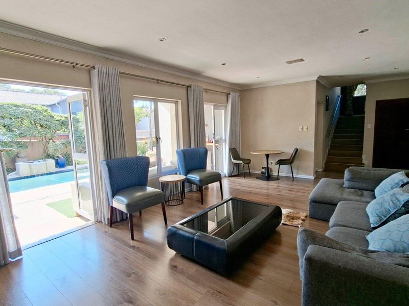 Spacious open-plan living area featuring laminate flooring, recessed lighting, and large sliding glass doors providing direct access to the outdoor pool area.