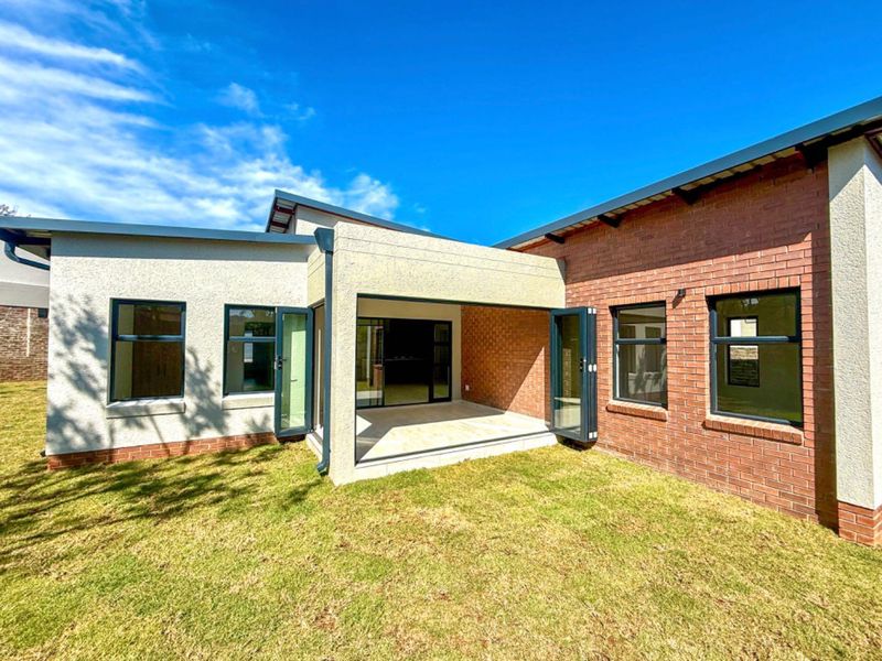 Rear view of the property featuring a covered patio with bi-fold doors, brick and plaster facade, and well-maintained lawn.