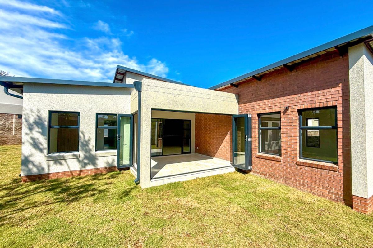 Rear view of the property featuring a covered patio with bi-fold doors, brick and plaster facade, and well-maintained lawn.