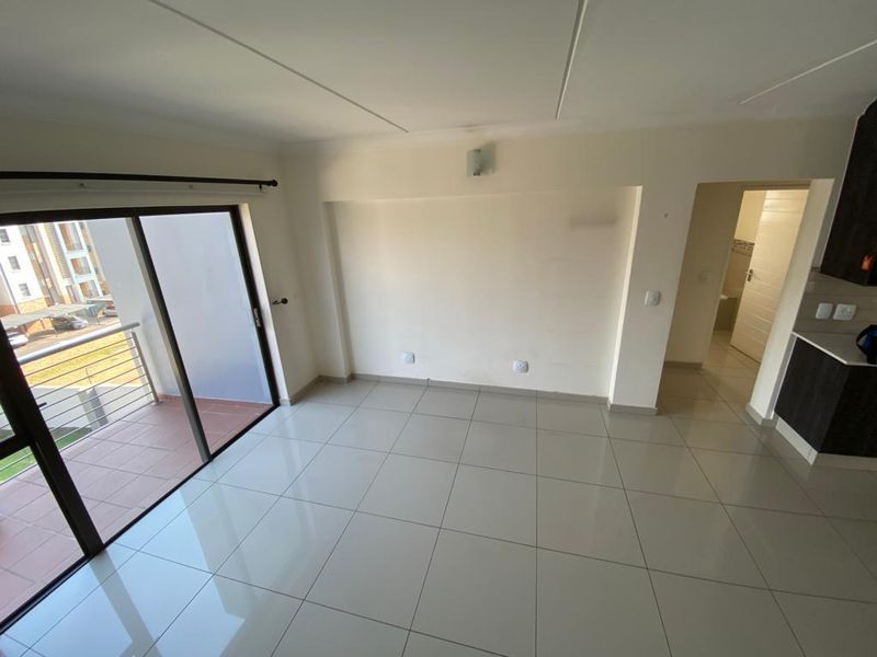An open-plan living area featuring tiled floors, a sliding door leading to a balcony, and an adjacent kitchen space.