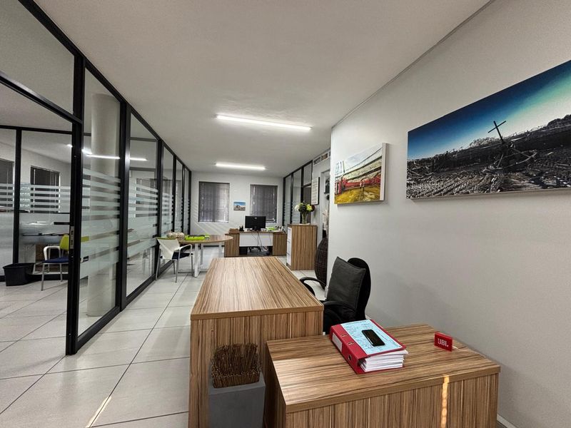 Modern office space featuring glass partition walls, tiled flooring, and efficient overhead lighting, providing a professional and well-lit work environment.