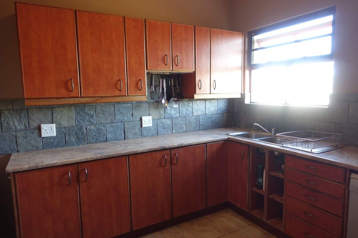 A functional kitchen featuring wooden cabinetry, stone-tiled backsplash, laminate countertops, and a double-basin sink with a window providing natural light.